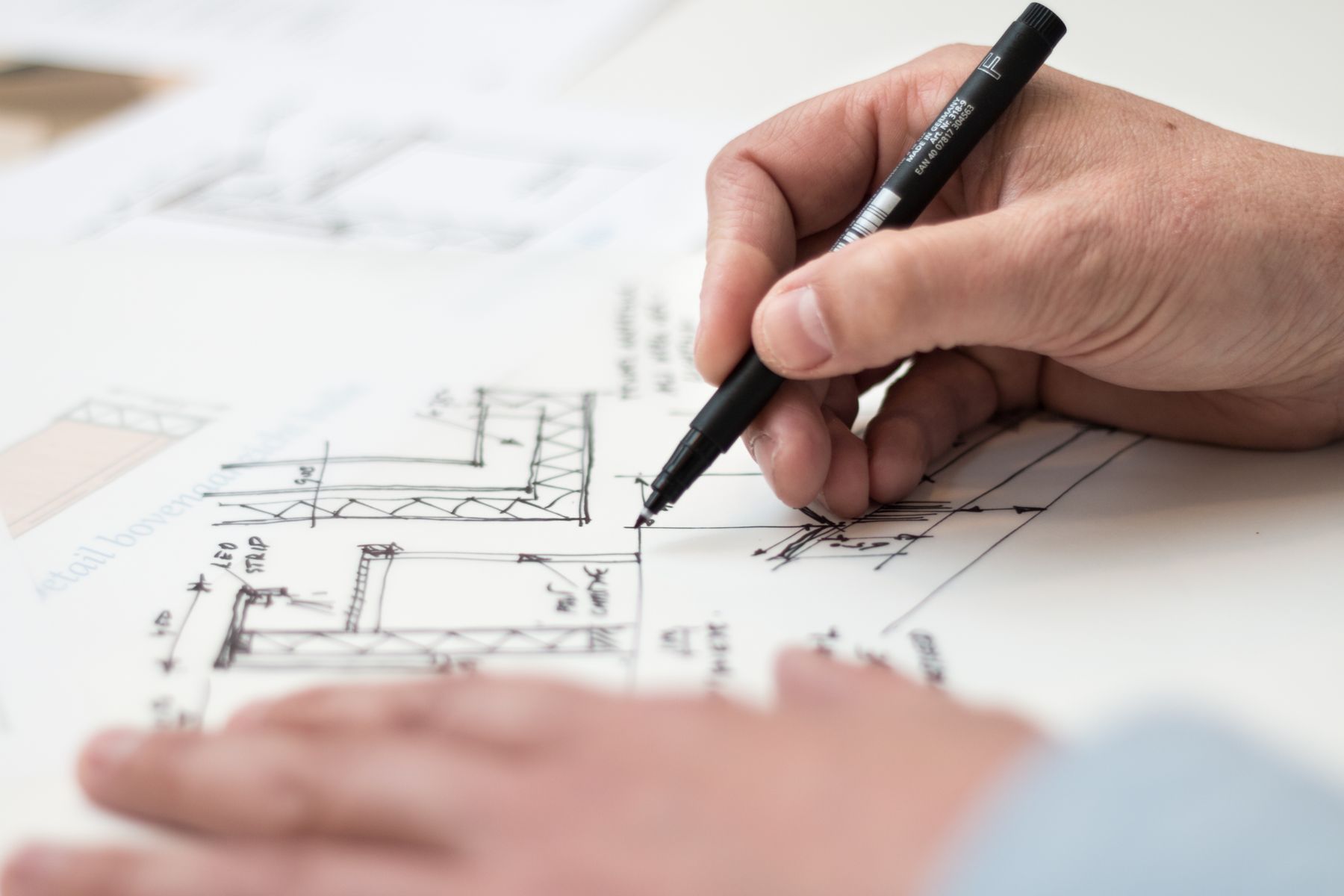 Architect drawing a detail by hand over a printed floor plan at a studio desk