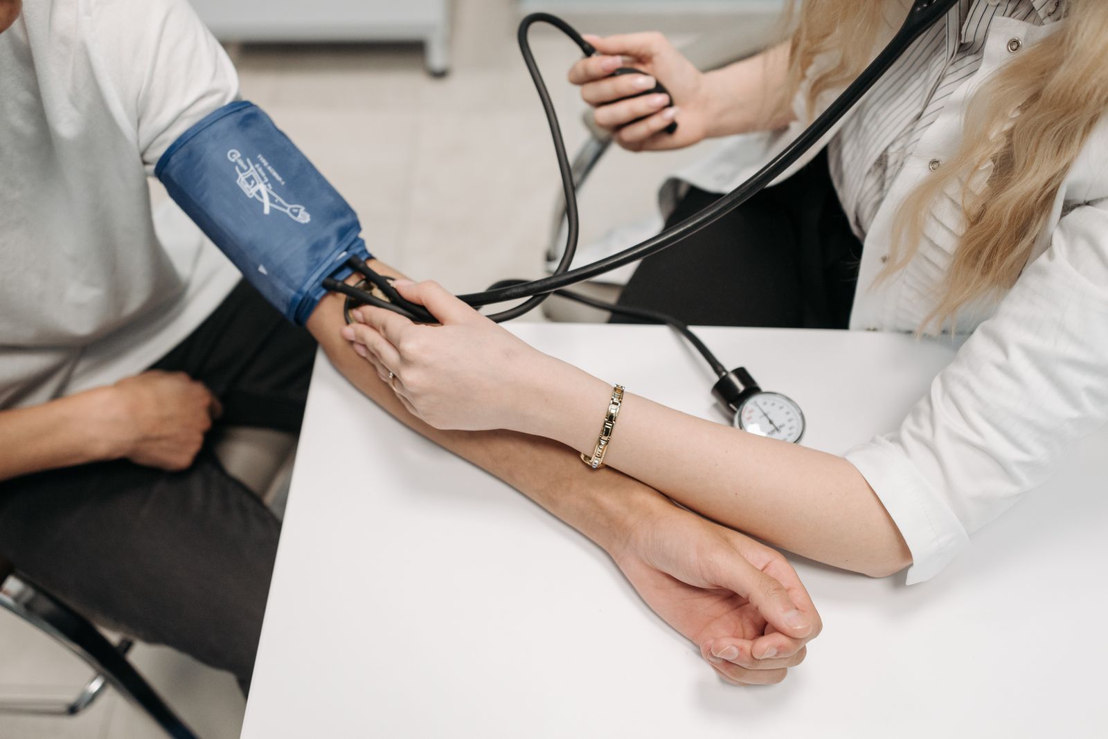 Clinician taking a seated patient's blood pressure reading with a cuff and stethoscope