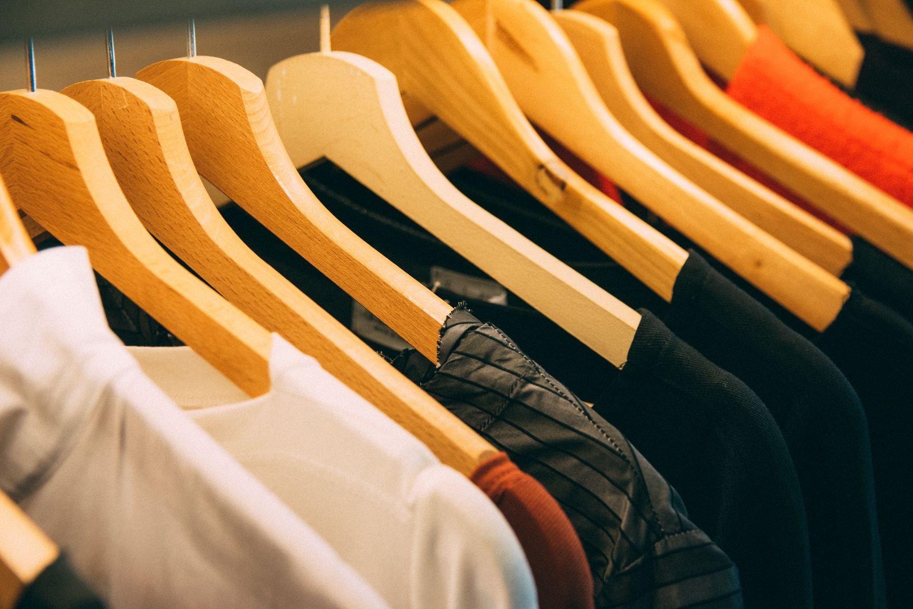 Garments on wooden hangers along a clothing rail