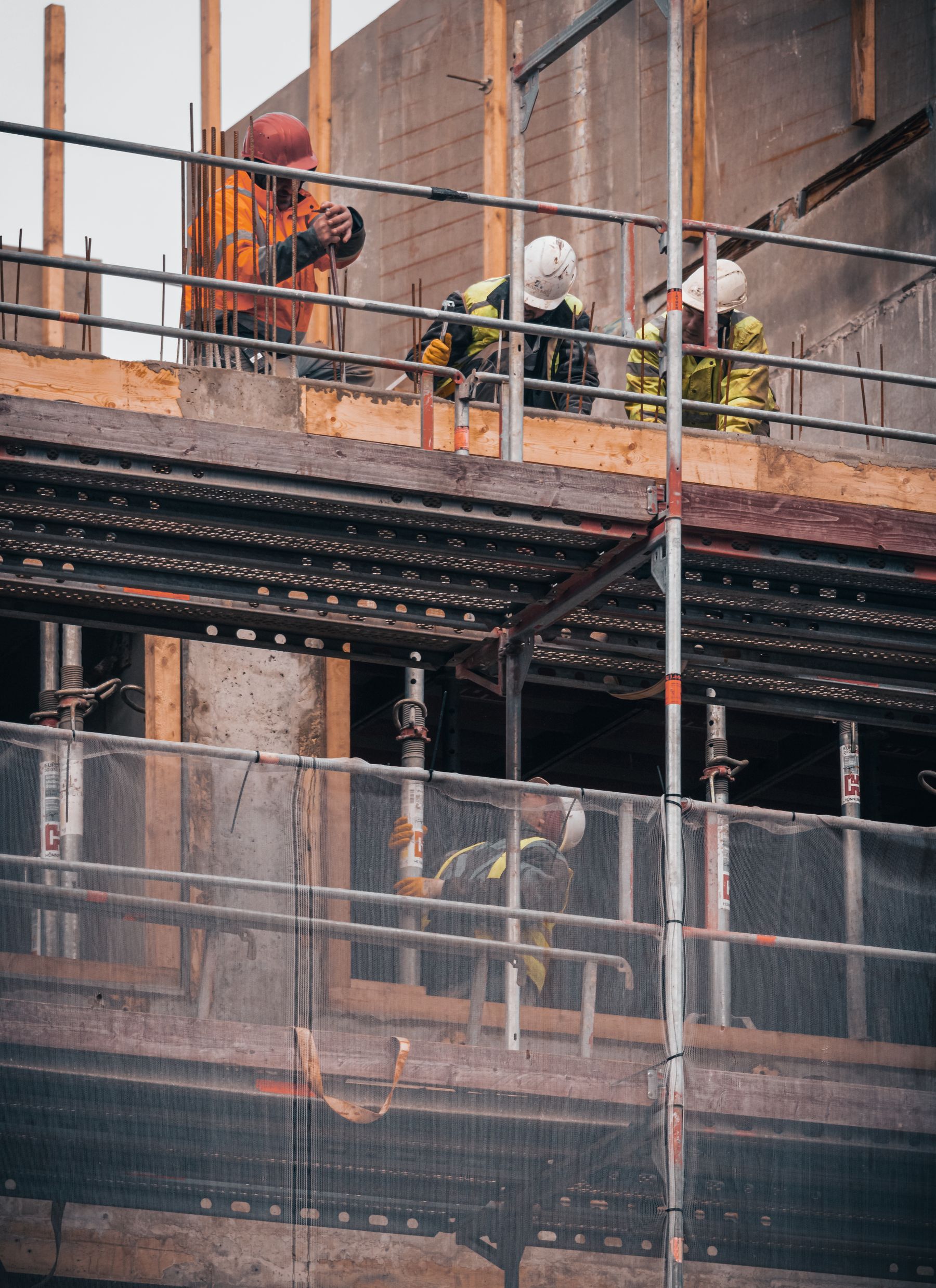 Construction workers in hard hats and safety gear working on concrete formwork at a building site