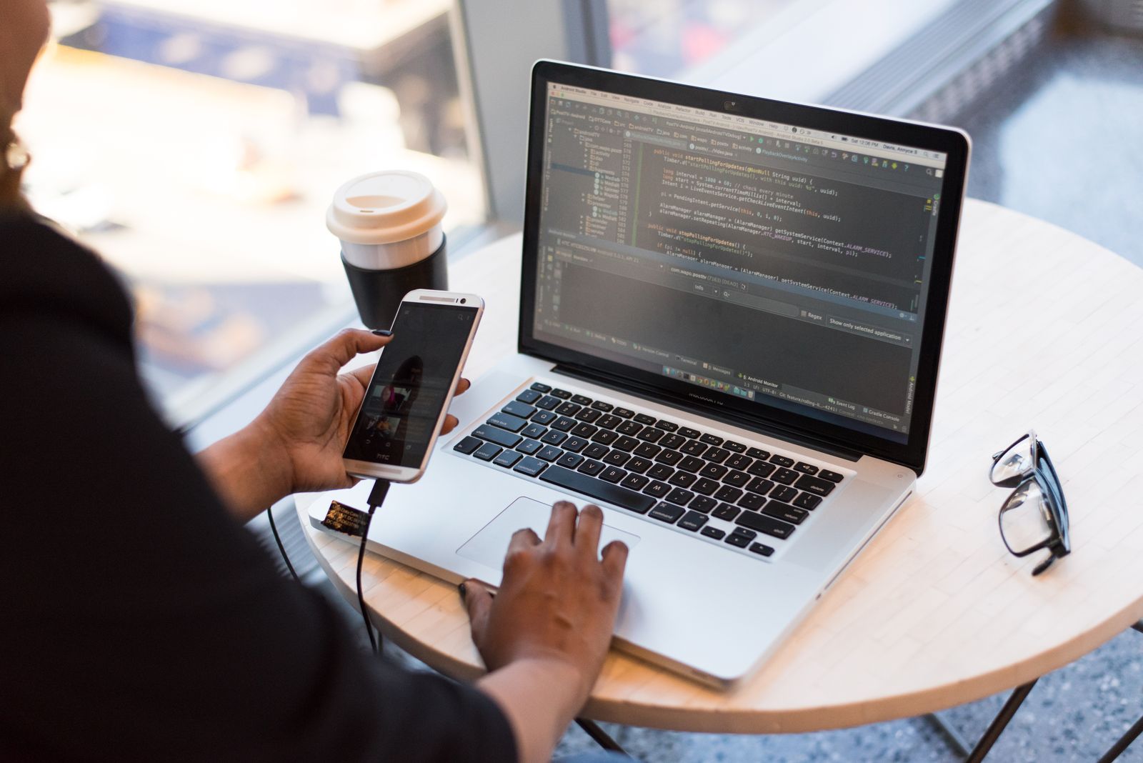 Person testing a product on a phone beside a laptop showing code at a desk