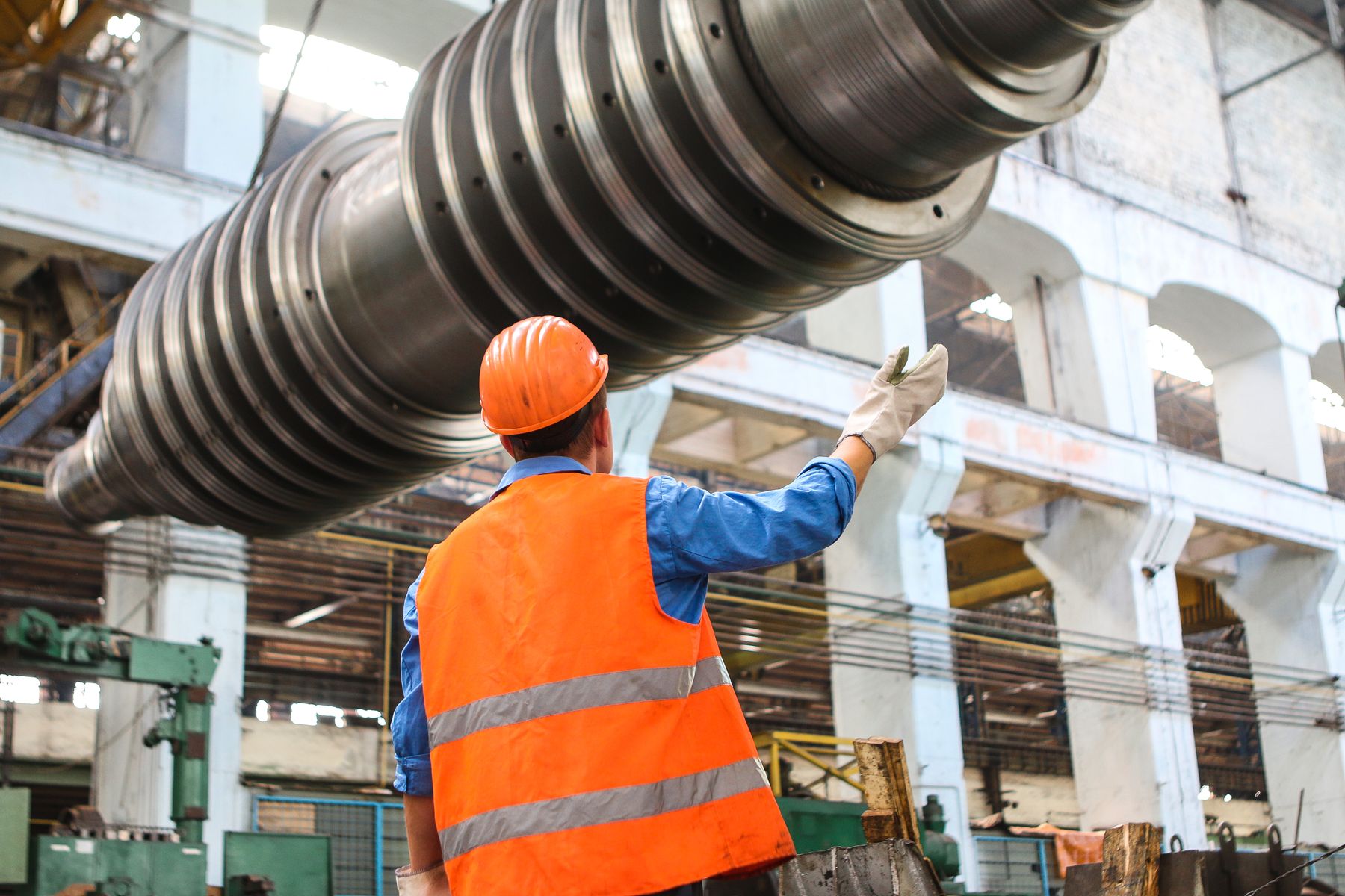 Engineer in high-visibility clothing inspecting a large machined industrial shaft