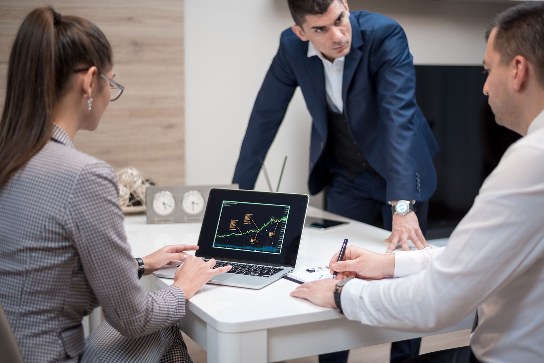 Three colleagues reviewing market charts on a laptop during a meeting in an office