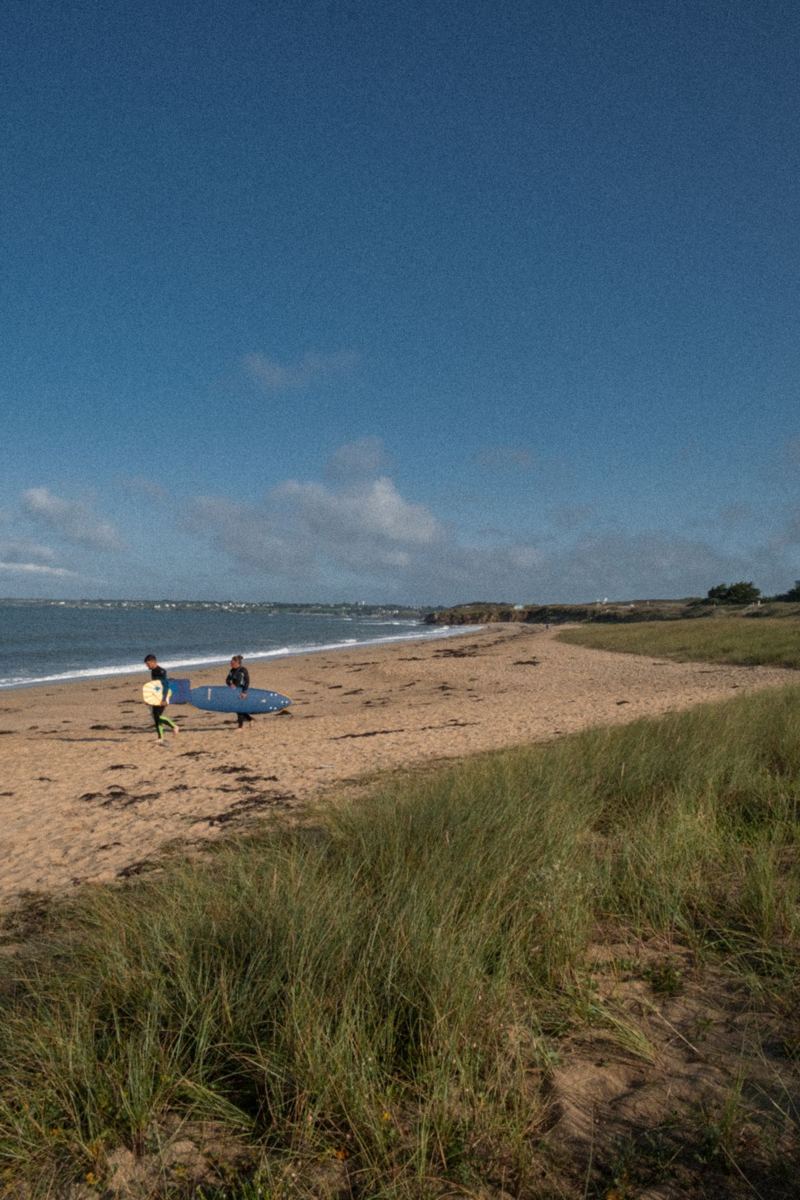 Surfers walking along a wide sandy beach